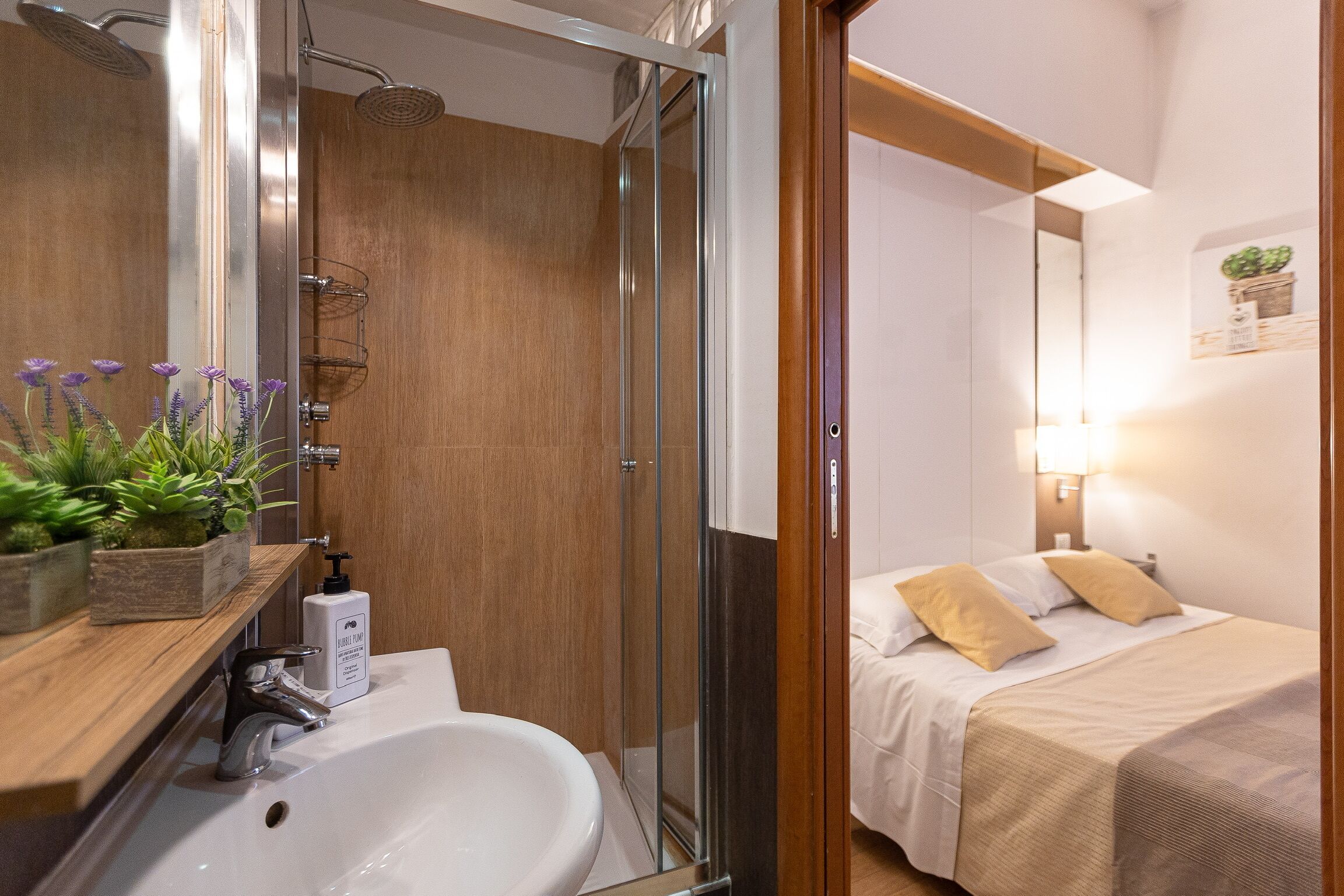 A modern bathroom with a shower, sink, and a bedside table with a plant.
