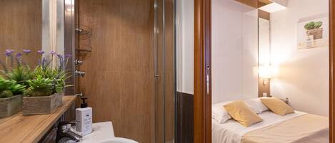 A modern bathroom with a shower, sink, and a bedside table with a plant.
