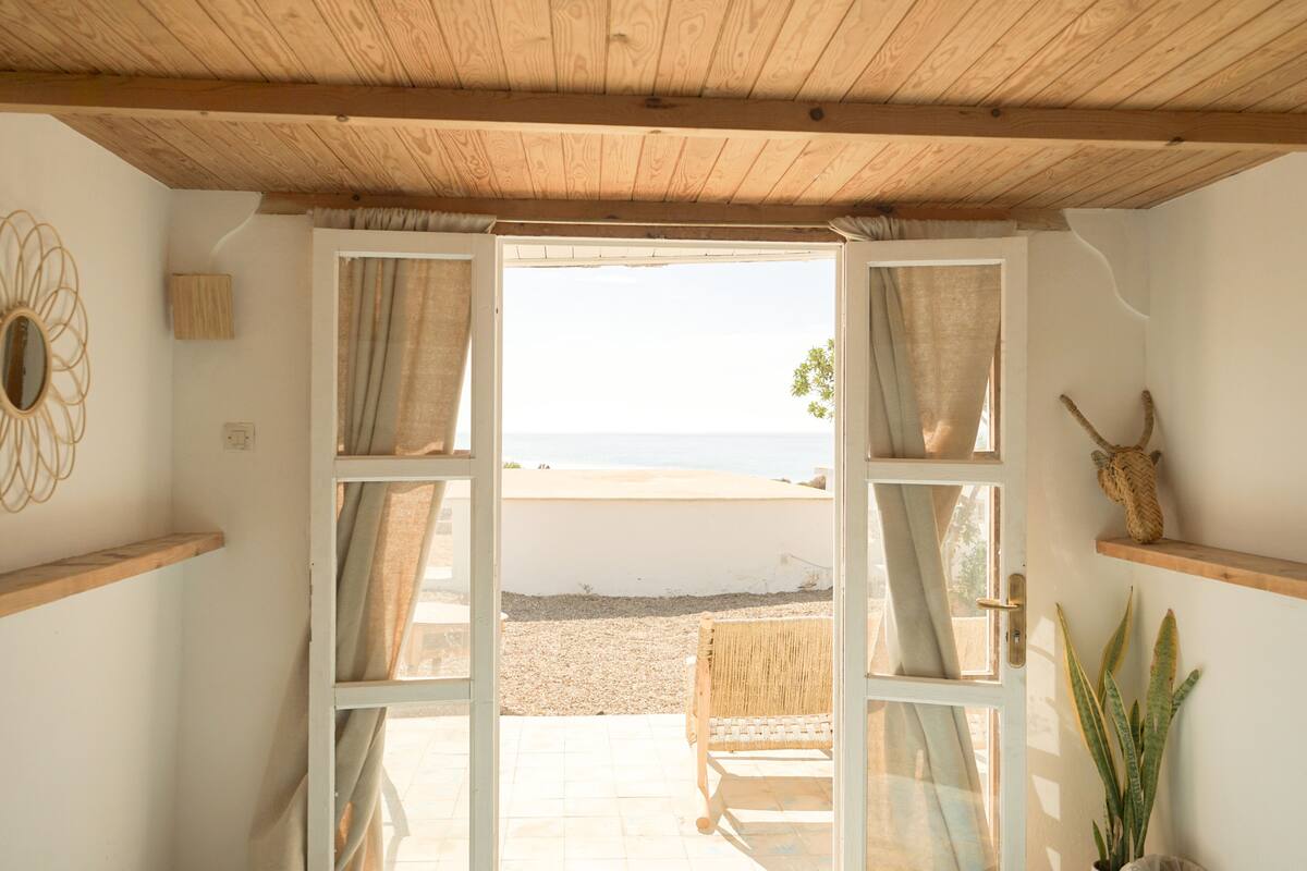 An open door leading to a beach view, with a wicker chair and a potted plant inside.