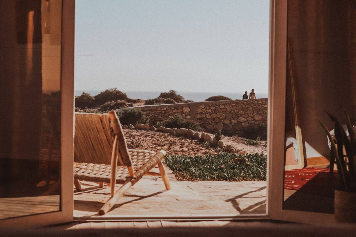 A room with a view of the sea, a stone wall, and a wicker chair.
