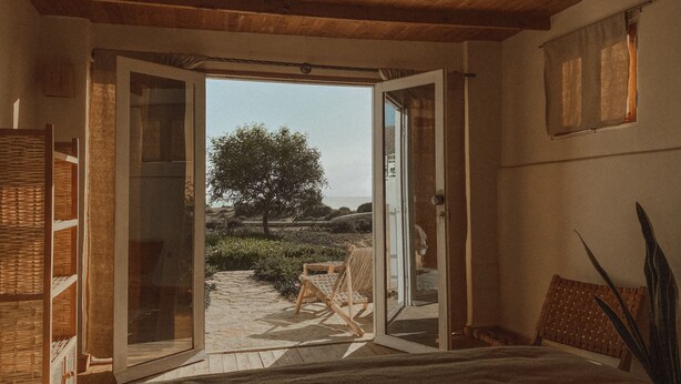 An open doorway leading to a garden with a tree, a wicker chair, and a bed with a view. - Dreamsea Surf Camp Imsouane (Imsouane)