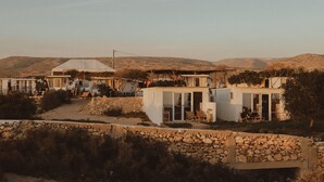 A series of white buildings with stone walls, some with glass doors and windows, set in a hilly landscape. - Dreamsea Surf Camp Imsouane (Imsouane)