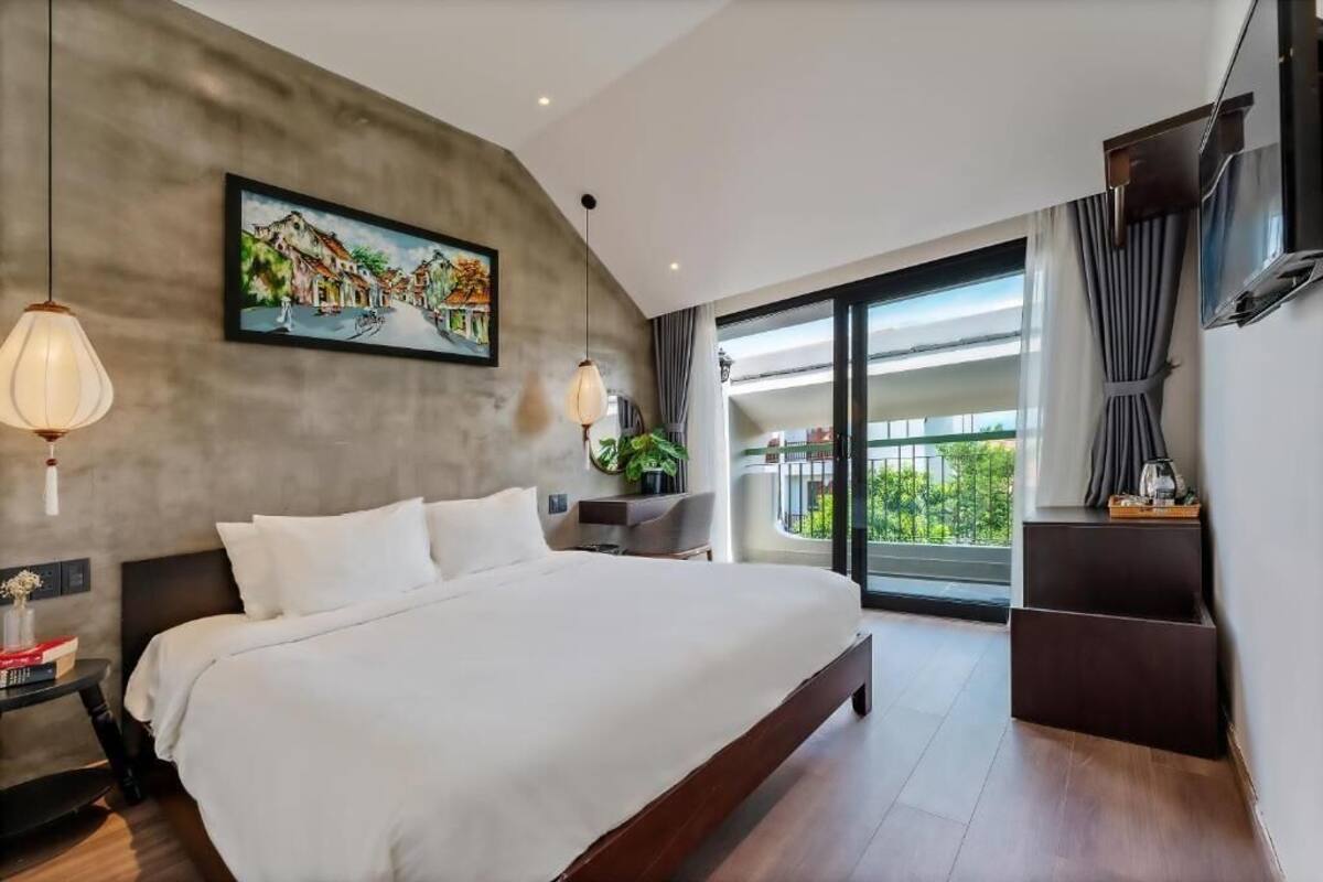 A modern hotel room with a large bed, a painting on the wall, a balcony with a view, and a TV mounted on the wall.