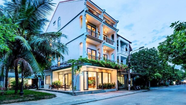 A multi-story hotel with a balcony on the second floor, a covered outdoor seating area, and a well-maintained garden. - Lacasa Old Town Villa (Da Nang)