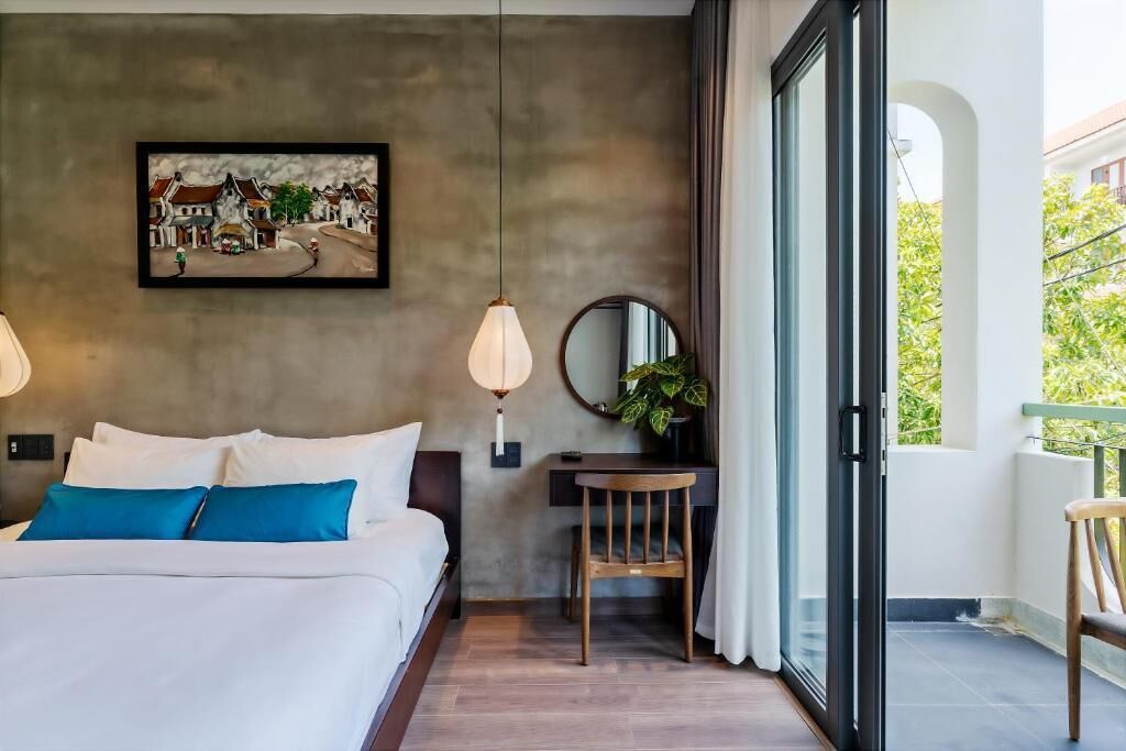 A bedroom with a bed, a desk, a chair, a hanging lamp, a mirror, and a window with a view of greenery.