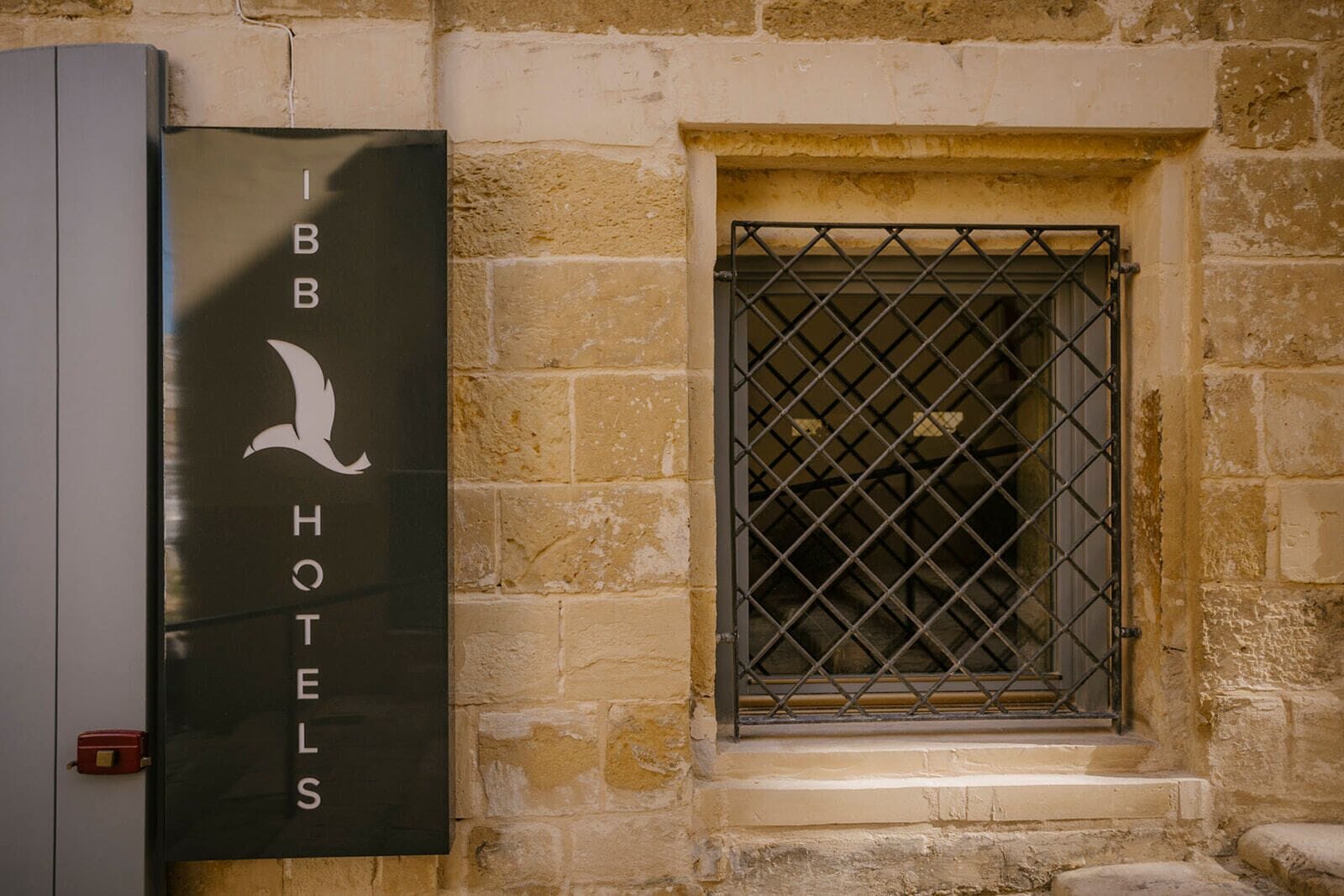 Een bord met 'IBB HOTELS', een vogel logo, een raam met metalen tralies en een stenen muur.