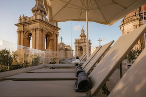 Terraço no telhado com cadeiras de descanso e guarda-sol, com vista para edifícios históricos de arquitetura elaborada.