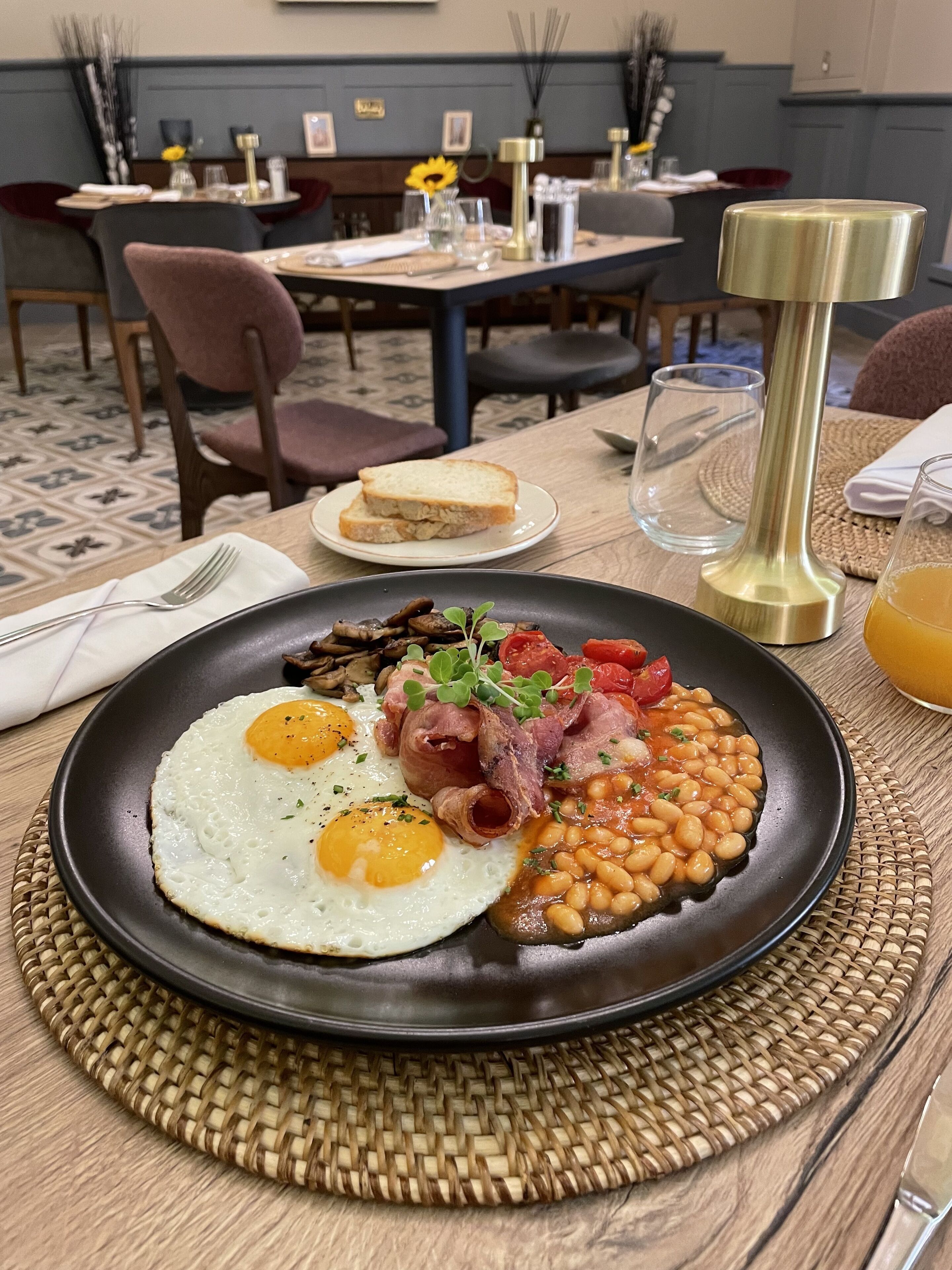 Un plato de desayuno con huevos, tocino, frijoles y tomates sobre un posavasos tejido.