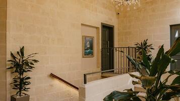 A spacious interior with a high ceiling, exposed wooden beams, a grand chandelier, a staircase, and potted plants.