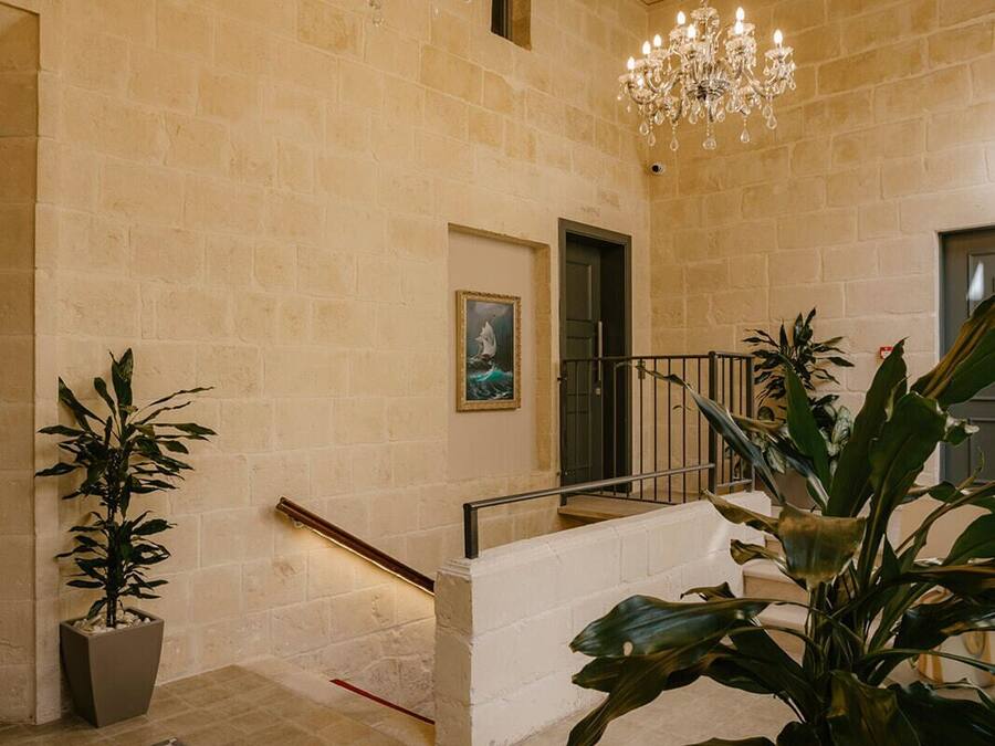 A spacious interior with a high ceiling, exposed wooden beams, a grand chandelier, a staircase, and potted plants.