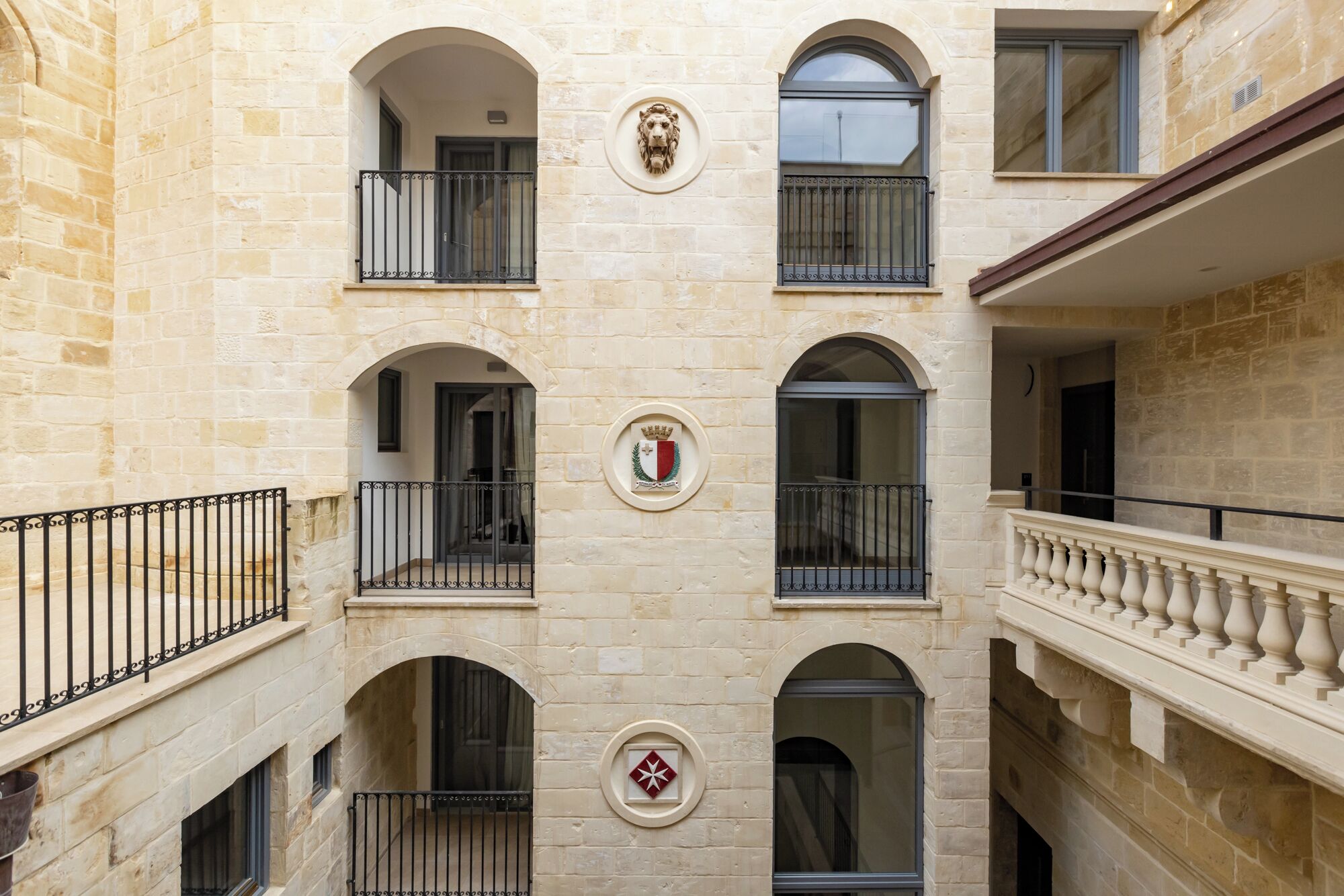 Un edificio de varios pisos con fachada de piedra, balcones con barandillas de hierro forjado y un escudo en la fachada.