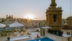 A rooftop pool area with a view of the cityscape and a prominent building with a dome. - IBB Hotel Palazzo Bettina Malta (Birgu)