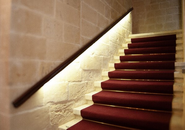 A staircase with red carpeted steps and a stone wall.