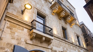 A stone building with a large arched entrance, a balcony with wrought iron railings, and a staircase leading to the entrance. - IBB Hotel Palazzo Bettina Malta (Birgu)