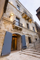 Un edificio de piedra con una gran entrada en arco, un balcón con barandilla de hierro forjado y una escalera que conduce a la entrada.