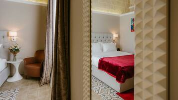 Habitación de hotel con cama, una silla, una mesita con un florero y una lámpara.