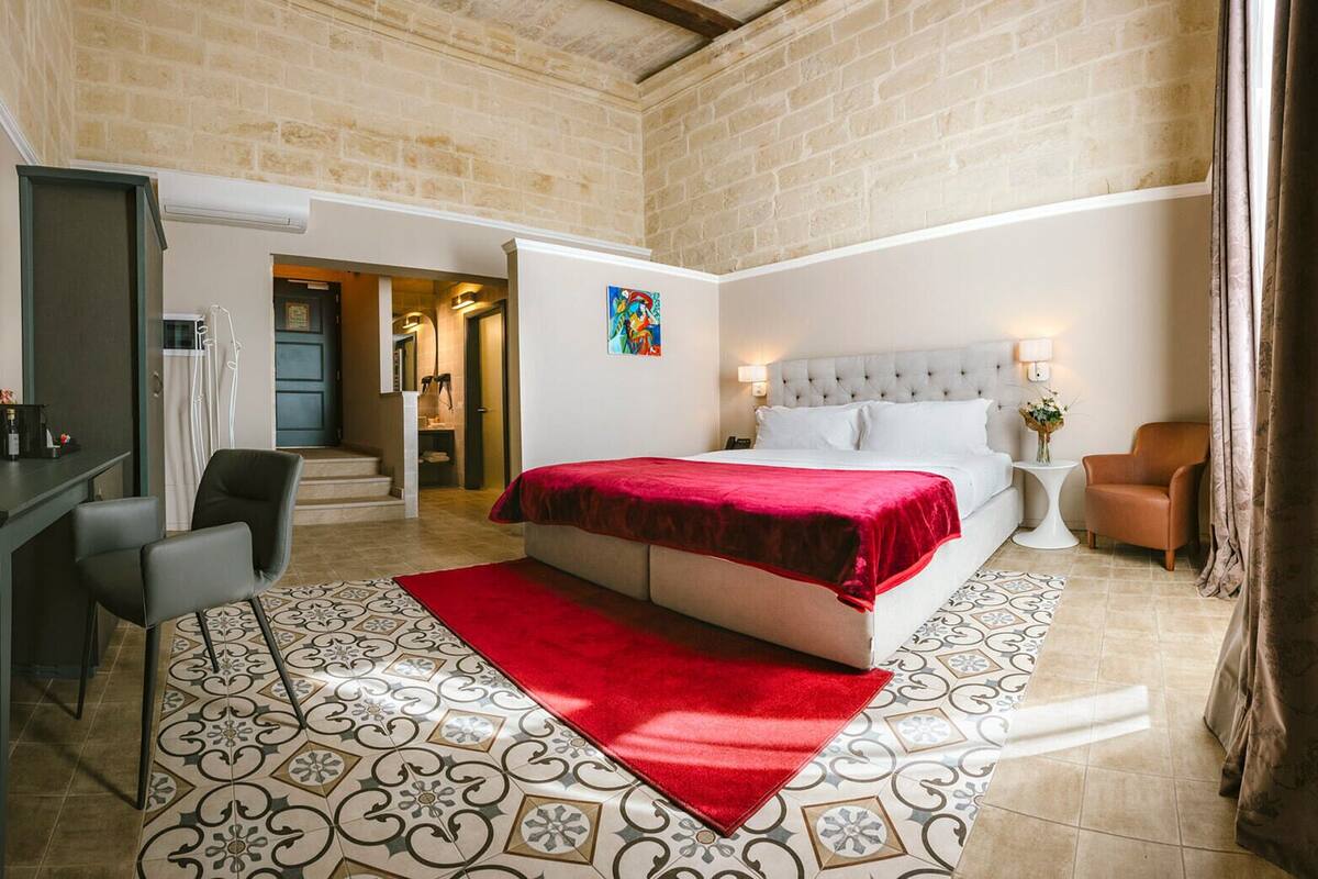 A bedroom with a bed, a desk, a chair, a nightstand, and a bathroom visible through an open door.