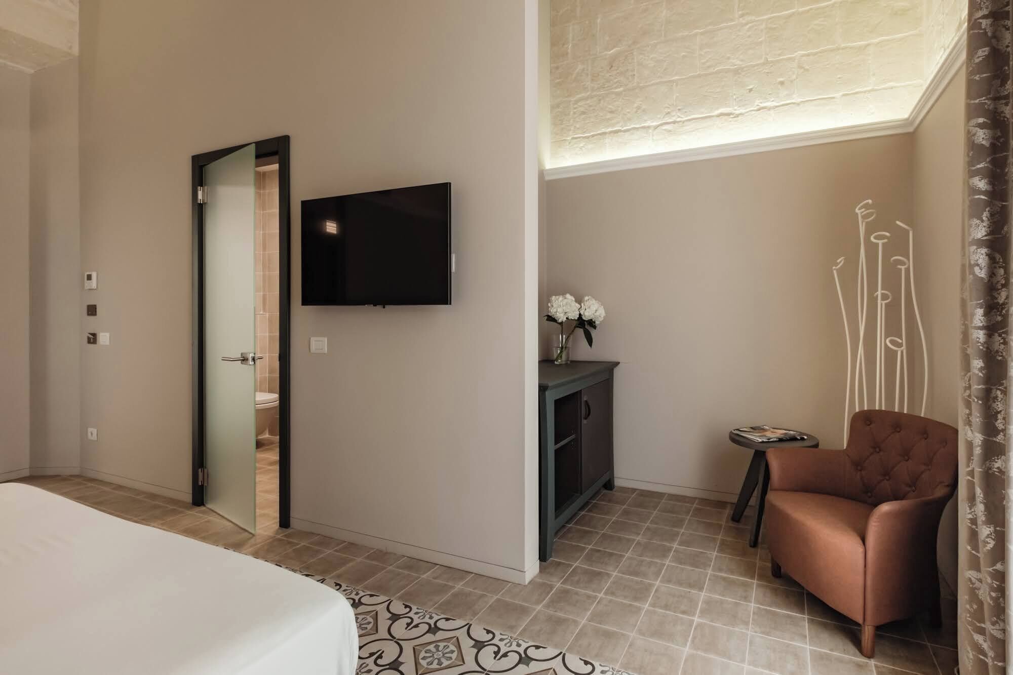 A hotel room with a bed, a television mounted on the wall, a small table with a vase of flowers, and a chair.