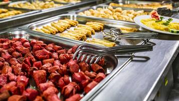 A buffet with various food items including sausages, rolled pasta, and a plate of scrambled eggs.