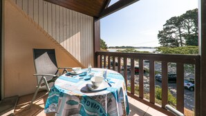 A balcony with a table set for dining, overlooking a parking area and trees.