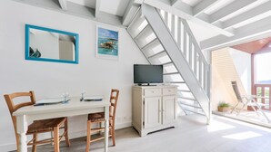 A dining area with a white table, two wooden chairs, a white cabinet with a television, and a blue-framed mirror.