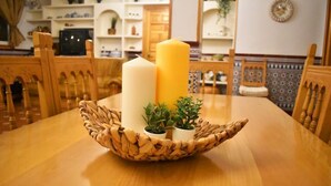 Une table à manger agrémentée d’un centre de table en fibres tressées, contenant des bougies et de petites plantes en pot.