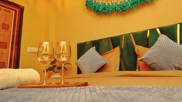 Hotelkamer met een bed, twee wijnglazen op een dienblad, een decoratieve wandhanger en een houten hoofdbord.
