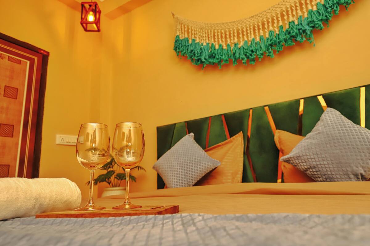 Une chambre d’hôtel avec un lit, deux verres à vin posés sur un plateau, une décoration murale et une tête de lit en bois.