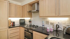 A modern kitchen with wooden cabinets, a gas stove, a microwave, and a kettle. - 5 Combehaven (Salcombe)