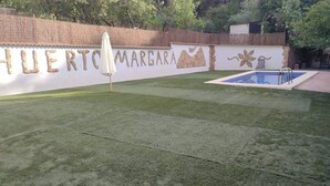 Un pati amb una piscina, una paret blanca amb el nom 'HURTO MARGARA' i elements decoratius, i un parasol blanc.