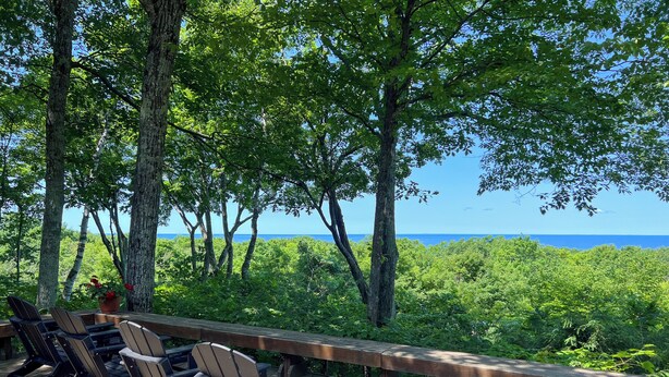 A wooden deck with Adirondack chairs overlooking a lush green landscape and a clear blue sky.