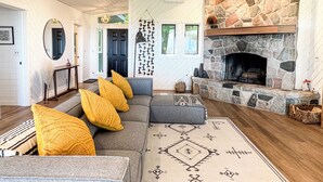 A living room with a stone fireplace, a gray sofa with yellow cushions, and a patterned rug.