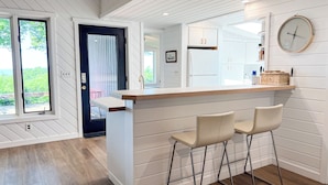 A modern kitchen with a bar area, wooden flooring, and a view through the door.