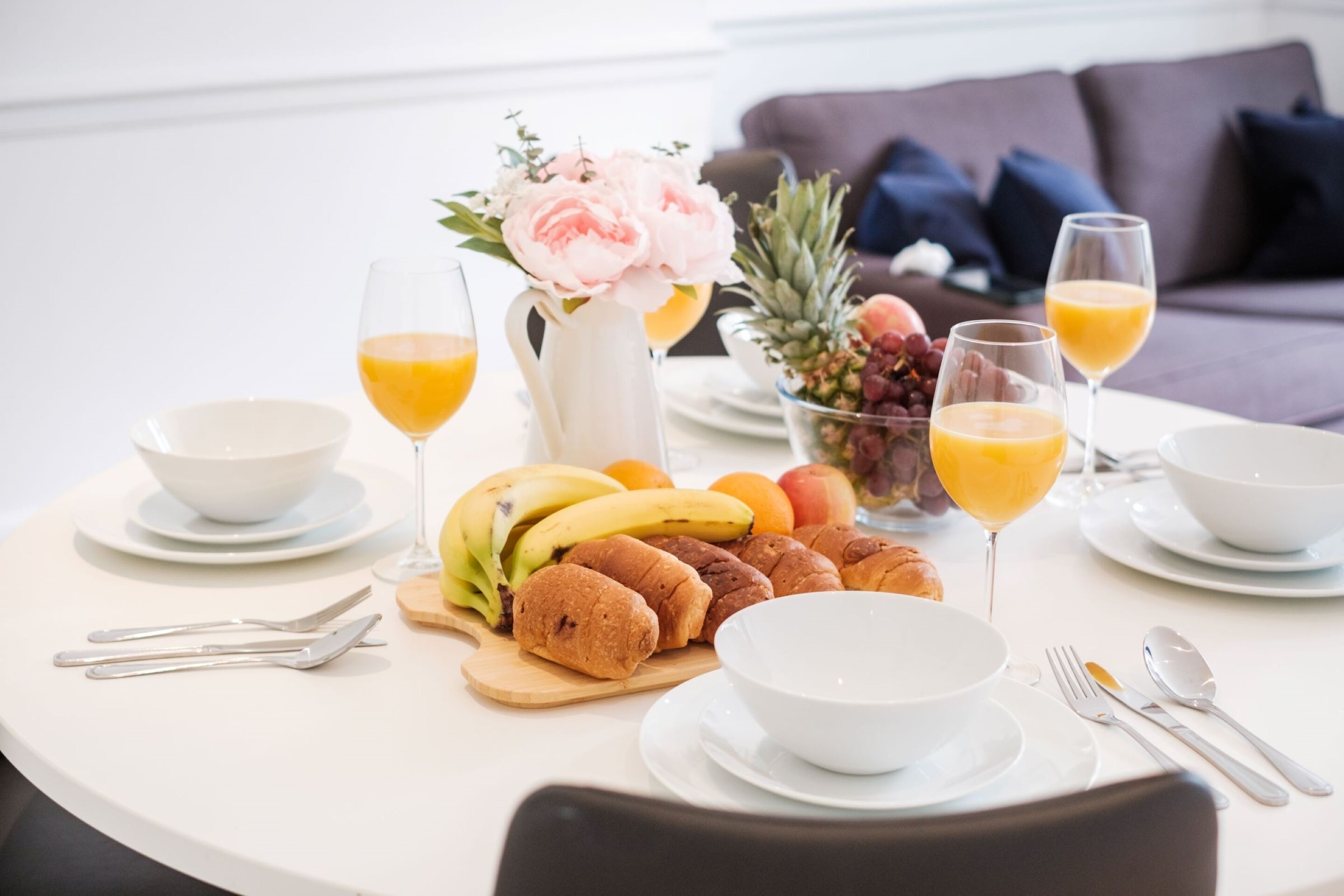 A breakfast table with fruits, pastries, and orange juice glasses.