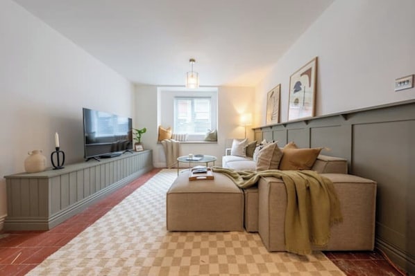 Ein modernes Wohnzimmer mit Sofa, Hocker, Fernseher und einem Schachbrettmuster-Teppich.