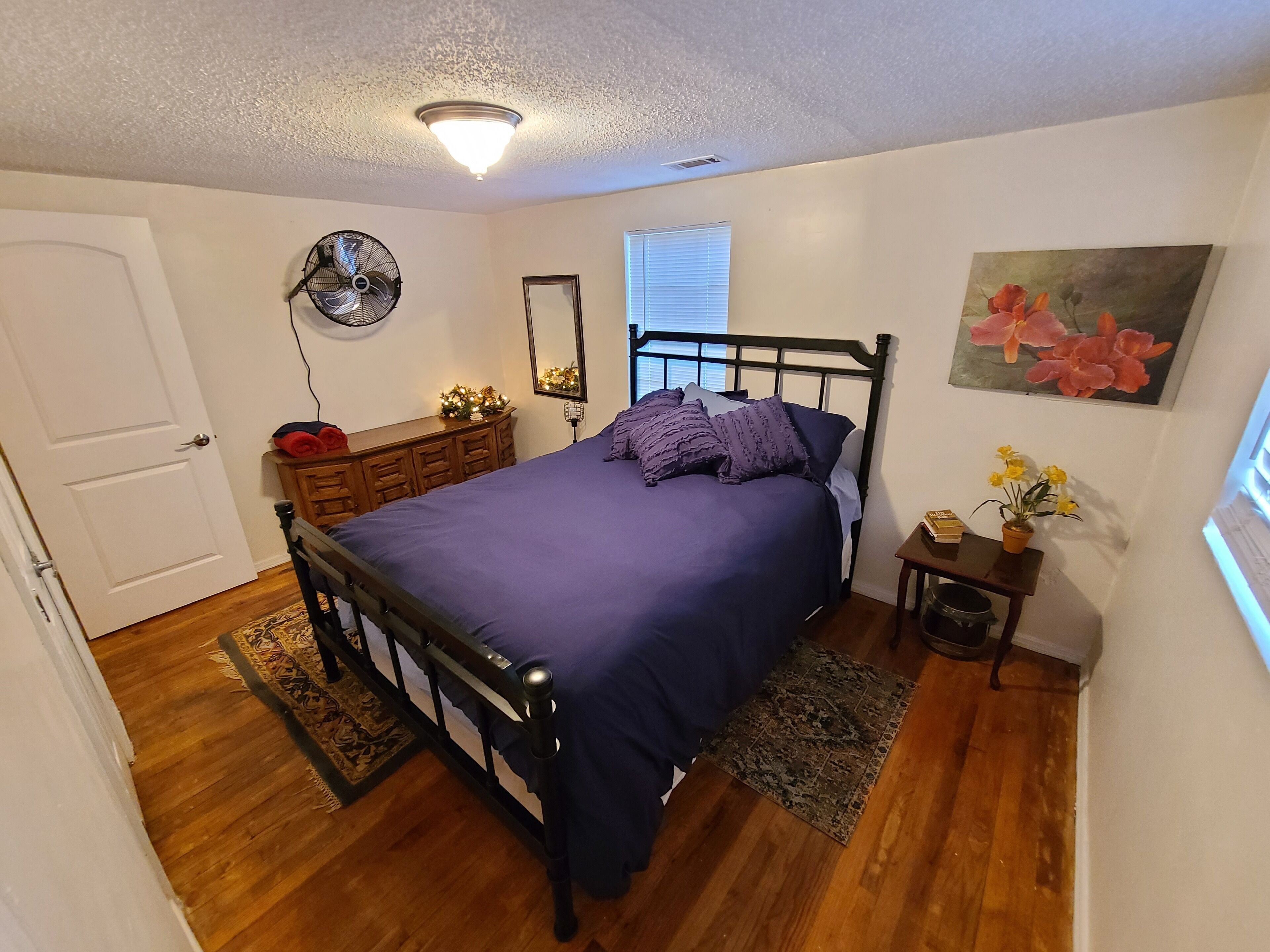 Een slaapkamer met een bed, een dressoir, een spiegel en een klein tafeltje met bloemen.