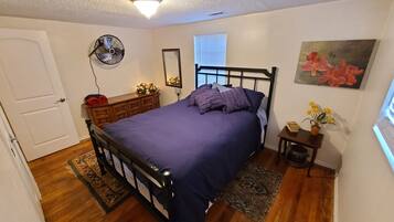 Een slaapkamer met een bed, een dressoir, een spiegel en een klein tafeltje met bloemen.