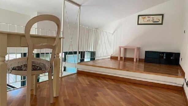 A spacious room with a wooden floor, a hanging chair, a small table, and a black cabinet.