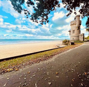 A beach with a stone tower, a paved walkway, and a clear sky.