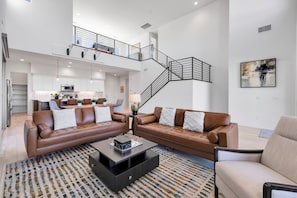 A spacious living area with a brown leather sofa set, a coffee table, and a patterned rug. A staircase with a metal railing leads to an upper level. - Sparkling New 3 Bed 3 Bath Private Pool Home With Incredible Views #260292 (La Quinta)