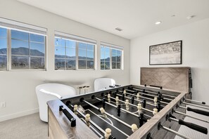 A room with a foosball table, large windows, a painting, and a view of mountains. - Sparkling New 3 Bed 3 Bath Private Pool Home With Incredible Views #260292 (La Quinta)
