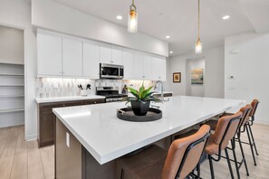 A modern kitchen with white cabinetry, stainless steel appliances, a central island with stools, and pendant lighting.