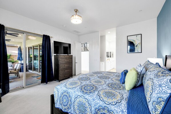 A bedroom with a large bed, a television, a wardrobe, and a sliding glass door leading to a balcony.