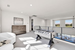 A modern living room with a foosball table, a sofa, and a view of a balcony.