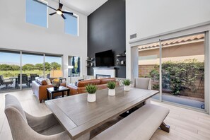 Un salon moderne doté d’une grande table à manger, de sièges confortables, d’un téléviseur à écran plat et offrant une vue sur l’extérieur.