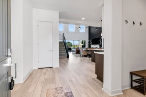 A spacious living area with a staircase leading to a balcony, a kitchen area with a large TV, and a dining space with a table and chairs.