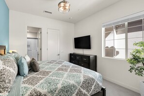 A bedroom with a bed, dresser, television, and a window.