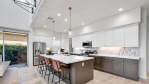 Una cocina moderna con una isla central, taburetes de bar y un comedor con banco.