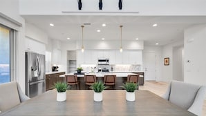 Una cocina moderna con armarios blancos, un refrigerador de acero inoxidable y una isla central con sillas.