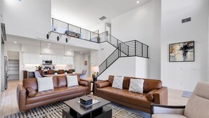 Amplia sala de estar con un sofá de cuero marrón, una mesa de centro y una escalera que conduce a un nivel superior.